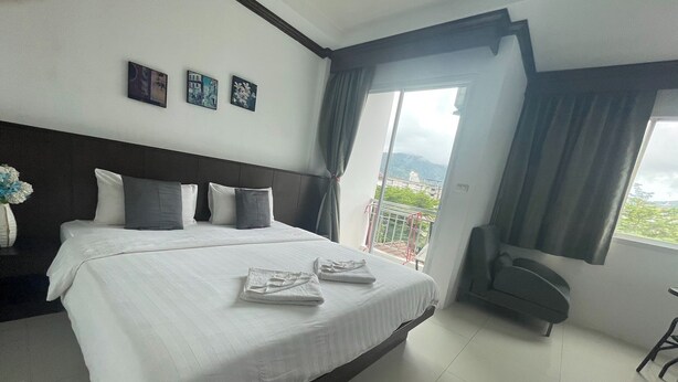 A hotel room with a large bed, a chair, a balcony with a view, and artwork on the wall. - Fruit Paradise Hotel (Patong)
