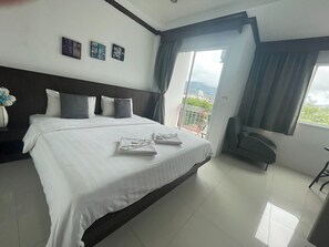 A hotel room with a large bed, a chair, a balcony with a view, and artwork on the wall. - Fruit Paradise Hotel (Patong)