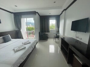 A hotel room with a bed, a desk, a TV, and a balcony with curtains. - Fruit Paradise Hotel (Patong)