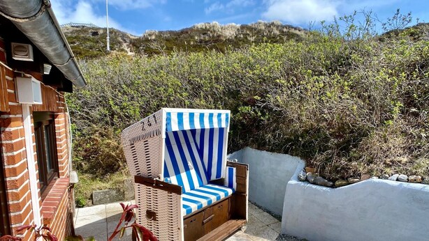 Una sedia in vimini con cuscino a righe blu e bianche, posta su un patio con vista su un paesaggio montuoso.