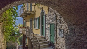 A stone building with a staircase leading to a balcony, a green door, and a view through an archway. - Casa Magnolia Varenna (Varenna)