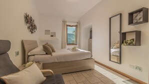 A bedroom with a bed, a chair, a mirror, and a window with a view of mountains. - Casa Magnolia Varenna (Varenna)