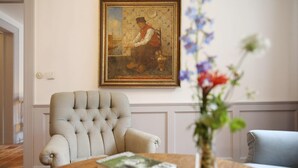 Una habitació amb un butac armchair amb guarniments, una taula de fusta amb un llibre, un ram de flors i un quadre emmarcat a la paret.