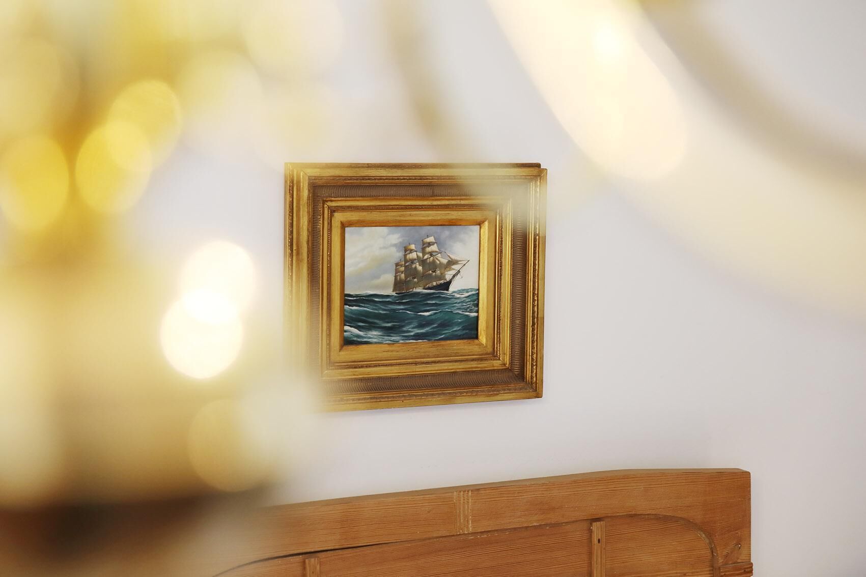 A framed painting of a ship on the sea on a white wall.