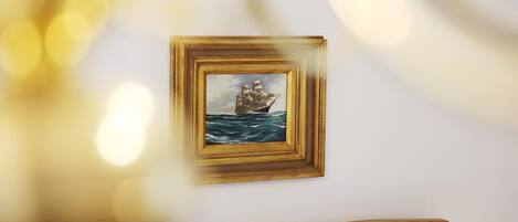 A framed painting of a ship on the sea on a white wall.