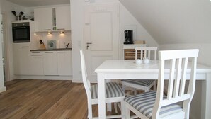 A kitchen with white cabinets, a white table, and striped chairs. - Top renovated apartment ideal for 3 persons (Hörnum auf Sylt)