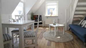 A modern, well-lit living room with a dining area, a blue sofa, and a staircase. - Top renovated apartment ideal for 3 persons (Hörnum auf Sylt)