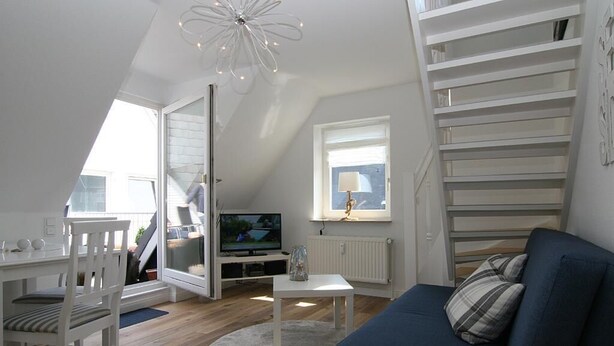A modern living room with a blue sofa, white furniture, a television, and a staircase. - Top renovated apartment ideal for 3 persons (Hörnum auf Sylt)