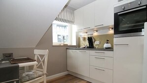 Cocina compacta con armarios blancos, horno negro y ventana con cortinas a rayas.