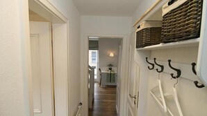 Un pasillo con piso de madera, paredes blancas y una puerta que da a una habitación.