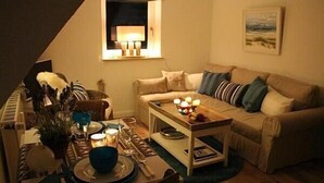 Una sala de estar acogedora con un sofá, una mesa de centro con velas y una zona de comedor con una mesa lista para dos.