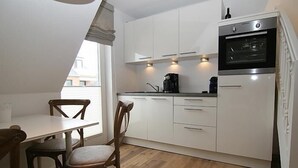 A compact kitchen with white cabinets, a built-in oven, and a dining area with wooden chairs and a table. - For a family of 4 or for two couples.... (Hörnum auf Sylt)