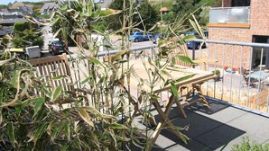 A balcony with a view of a residential street, a wooden bench, and a metal railing. - For a family of 4 or for two couples.... (Hörnum auf Sylt)