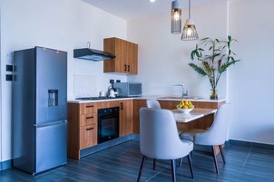 Una cocina moderna con refrigerador de acero inoxidable, gabinetes de madera, microondas y un comedor con dos sillas y un frutero.