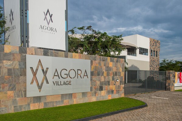 A modern building with a stone facade and a sign reading "Agora Village." - Agora Apartments (Lusaka)