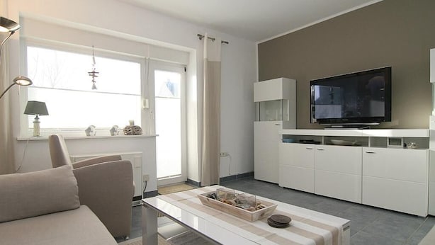 Ett modernt vardagsrum med en soffa, ett soffbord, en platt-TV och en köksdel med skåp och en mikrovågsugn.