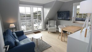 A modern living room with a blue sofa, a small white table, a striped armchair, and a wooden dining table.