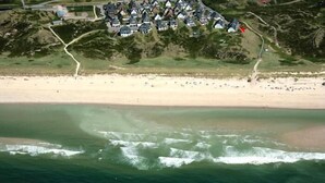 An aerial view of a coastal area with a beach and a cluster of houses.