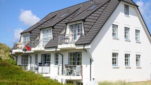 A two-story house with a sloped roof, multiple windows, and a balcony with outdoor furniture.