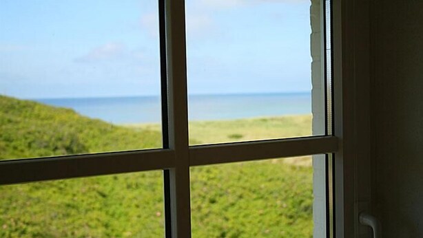 A window with a view of a grassy landscape and a body of water.