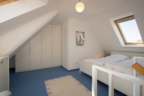Une chambre avec un plafond en pente, un lit, une armoire, une petite table, une table de chevet, une lampe, une affiche et une fenêtre.