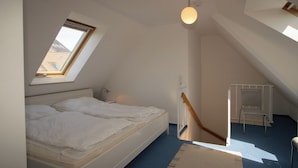 Quarto com claraboia, cama, escrivaninha e cadeira.