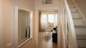 A hallway with a staircase, a door with frosted glass, a small table, and a painting on the wall.