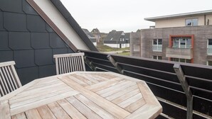 A wooden table and chairs on a balcony with a view of neighboring buildings.