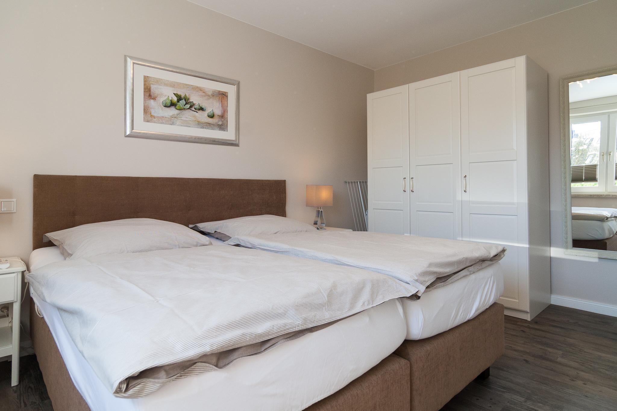 Ein Doppelbett mit weißen Leinen, ein Nachttisch, eine Nachttischlampe, ein gerahmtes Kunstwerk an der Wand und ein großer weißer Kleiderschrank.