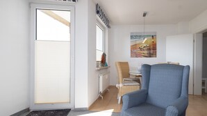 Uma sala de estar moderna com uma poltrona azul, uma mesa de jantar com cadeiras, um radiador e uma janela com persianas.