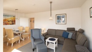 Sala de estar com sofá, poltronas, mesa de jantar com cadeiras, mesinha lateral e luminária pendente.