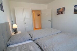 Une chambre à coucher comprenant un lit, une table de chevet avec une lampe, une armoire et une porte donnant sur une autre pièce.
