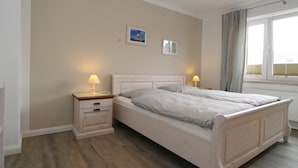 A bedroom with a bed, bedside tables, and a window with curtains. - Fantastic vacation apartment in Hörnum for 4 people - pure relaxation! (Hörnum auf Sylt)