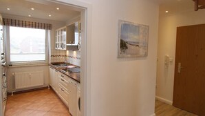A kitchen with white cabinets, a built-in oven, and a window with blinds. - Fantastic vacation apartment in Hörnum for 4 people - pure relaxation! (Hörnum auf Sylt)