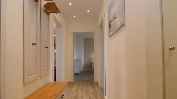 A narrow hallway with wooden flooring, white walls, and a wooden bench. - Fantastic vacation apartment in Hörnum for 4 people - pure relaxation! (Hörnum auf Sylt)