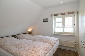 Ein Schlafzimmer mit zwei Betten, einem Fenster mit Jalousien, einem Heizkörper und einem kleinen Bild an der Wand.
