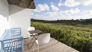 Eine Holzterrasse mit einem Reetdach, einem weißen Stuhl, einem blauen Stuhl und einem kleinen Tisch.