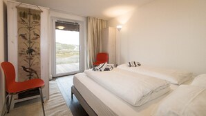 Ein Hotelzimmer mit zwei Betten, einem roten Sessel, einem Fenster mit Vorhängen und Blick ins Freie.