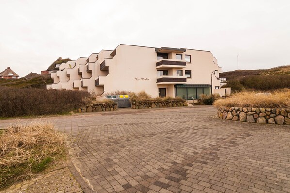 Een modern gebouw met een opvallende, in een zigzagpatroon vormgegeven gevel, een stenen muur-entree en een verharde oprit.
