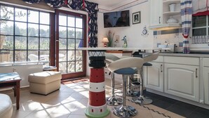 Una cocina con armarios blancos, un taburete de bar, una mesa con forma de faro y vistas al exterior.