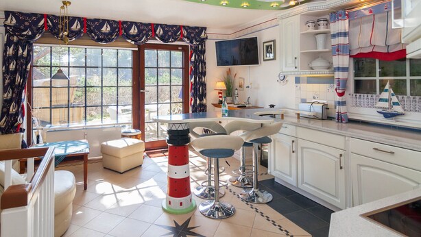 Una cocina con temática náutica, con un amplio ventanal, una decoración con faro y una zona de bar.