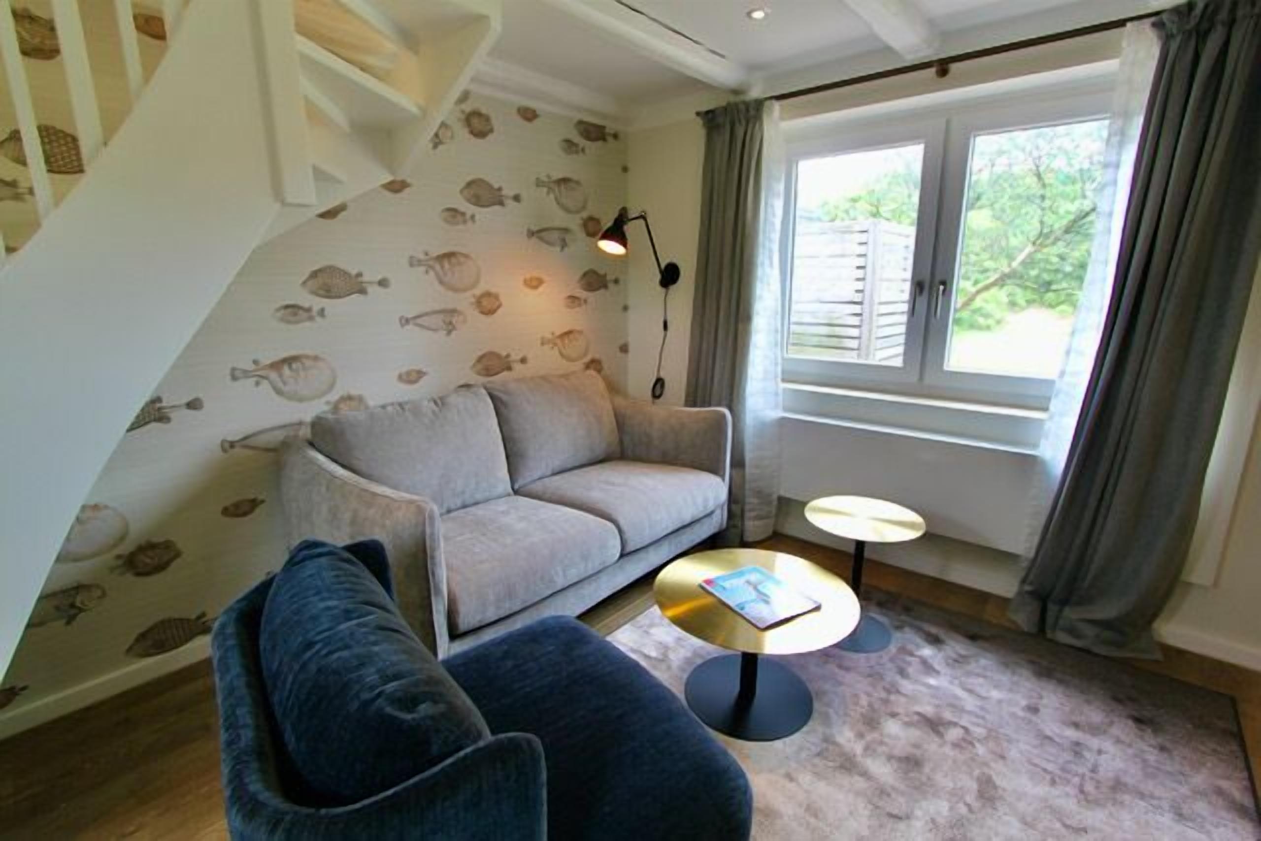 A cozy living room with a sofa, a chair, a small round table, and a staircase with a fish-patterned wall.