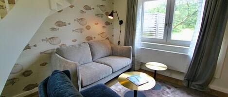 A cozy living room with a sofa, a chair, a small round table, and a staircase with a fish-patterned wall.
