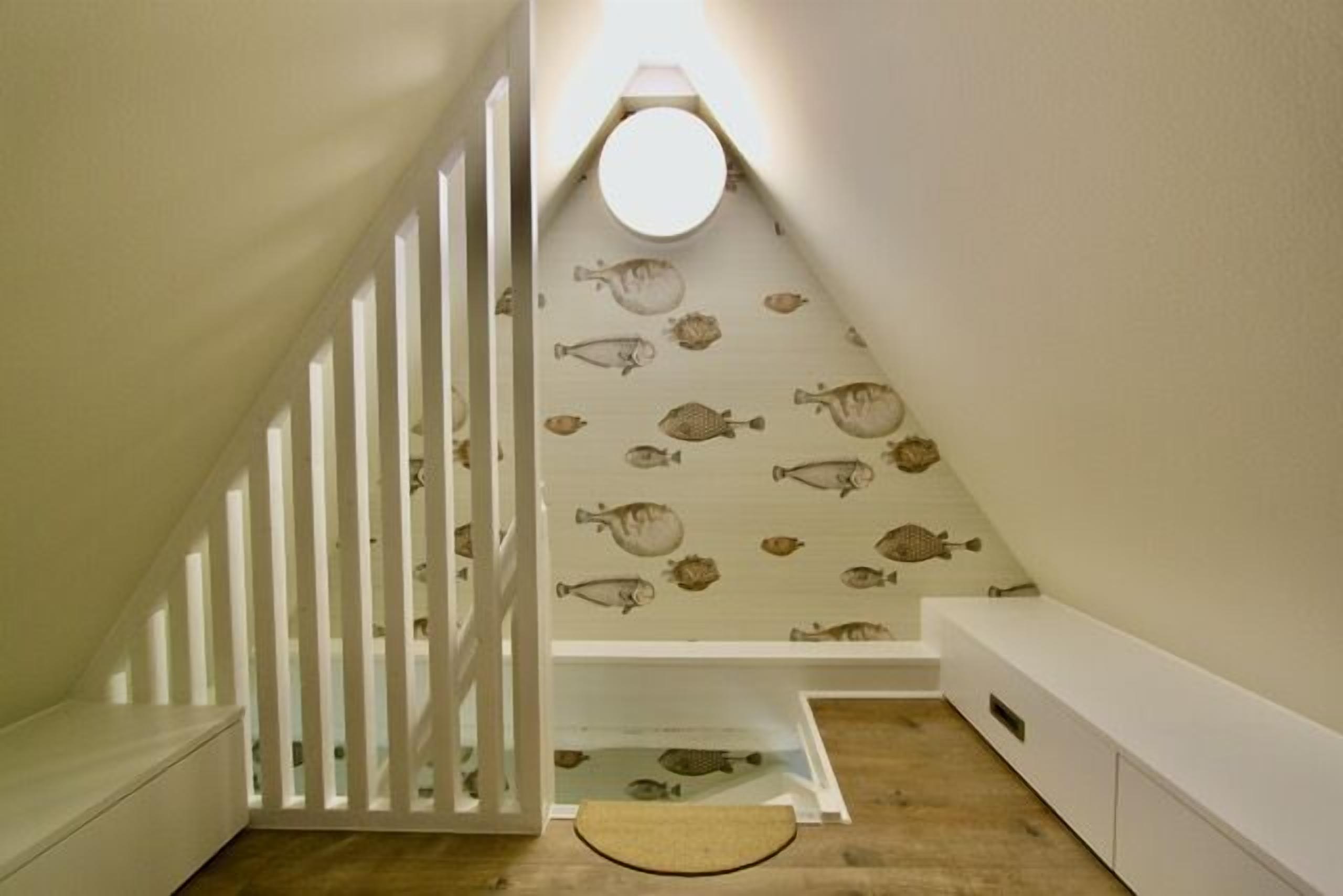 Una escalera estrecha con barandilla blanca, piso de madera y pared decorada con motivos de peces.
