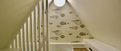 Una escalera estrecha con barandilla blanca, piso de madera y pared decorada con motivos de peces.