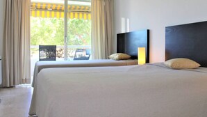 Une chambre d’hôtel avec deux lits, une grande fenêtre avec des rideaux, un téléviseur à écran plat et une vue sur la verdure environnante.