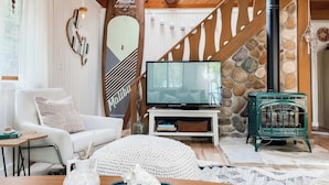 Ein gemütliches Wohnzimmer mit einem weißen Sofa, einem Fernseher, einer Steinwand und einem grünen Kamin.