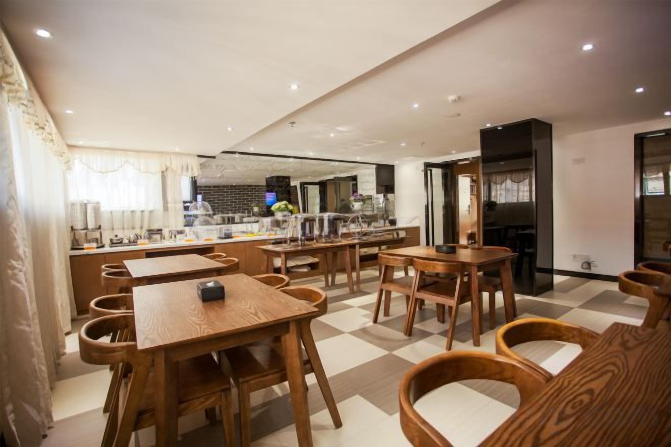 Un restaurante con mesas y sillas de madera, una zona de cocina y un suelo a cuadros.