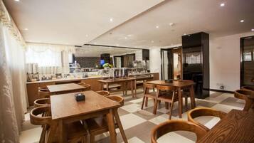 Un restaurante con mesas y sillas de madera, una zona de cocina y un suelo a cuadros.
