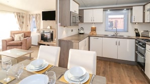 Una cocina moderna con armarios blancos, un microondas y una estufa. Hay un comedor con una mesa dispuesta para dos personas, y un televisor montado en la pared.